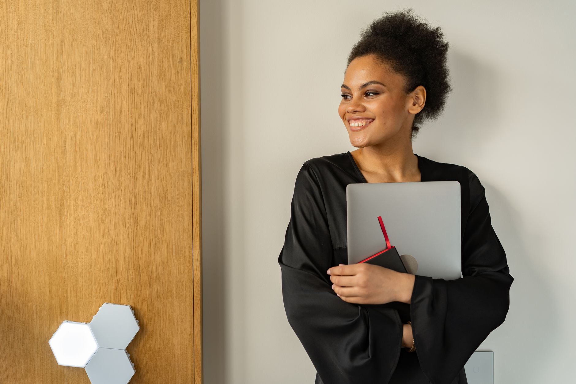 Vrouw met afro-kapsel houdt lachend een laptop vast, thuiskantoor.